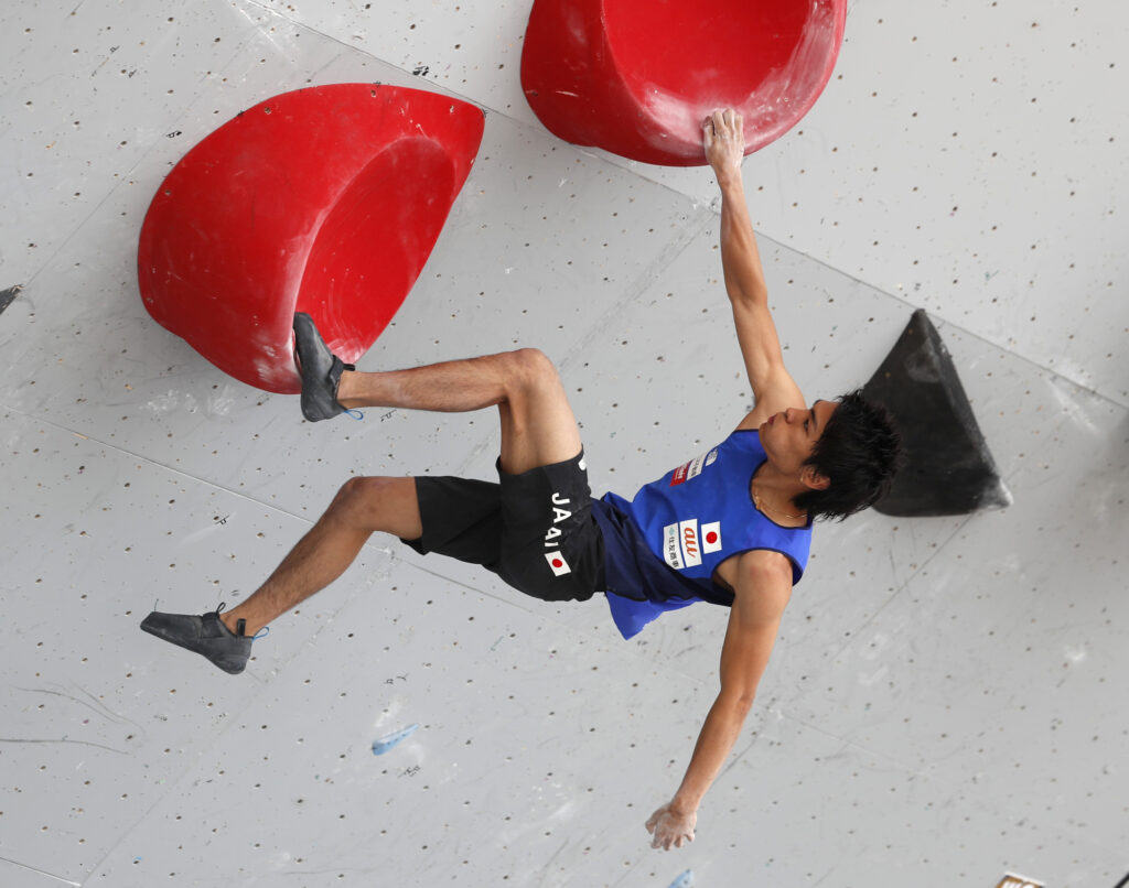 tomoa narasaki doing a dynamic move on a competition wall. He also has a long wingspan, with his ape index being +10cm!